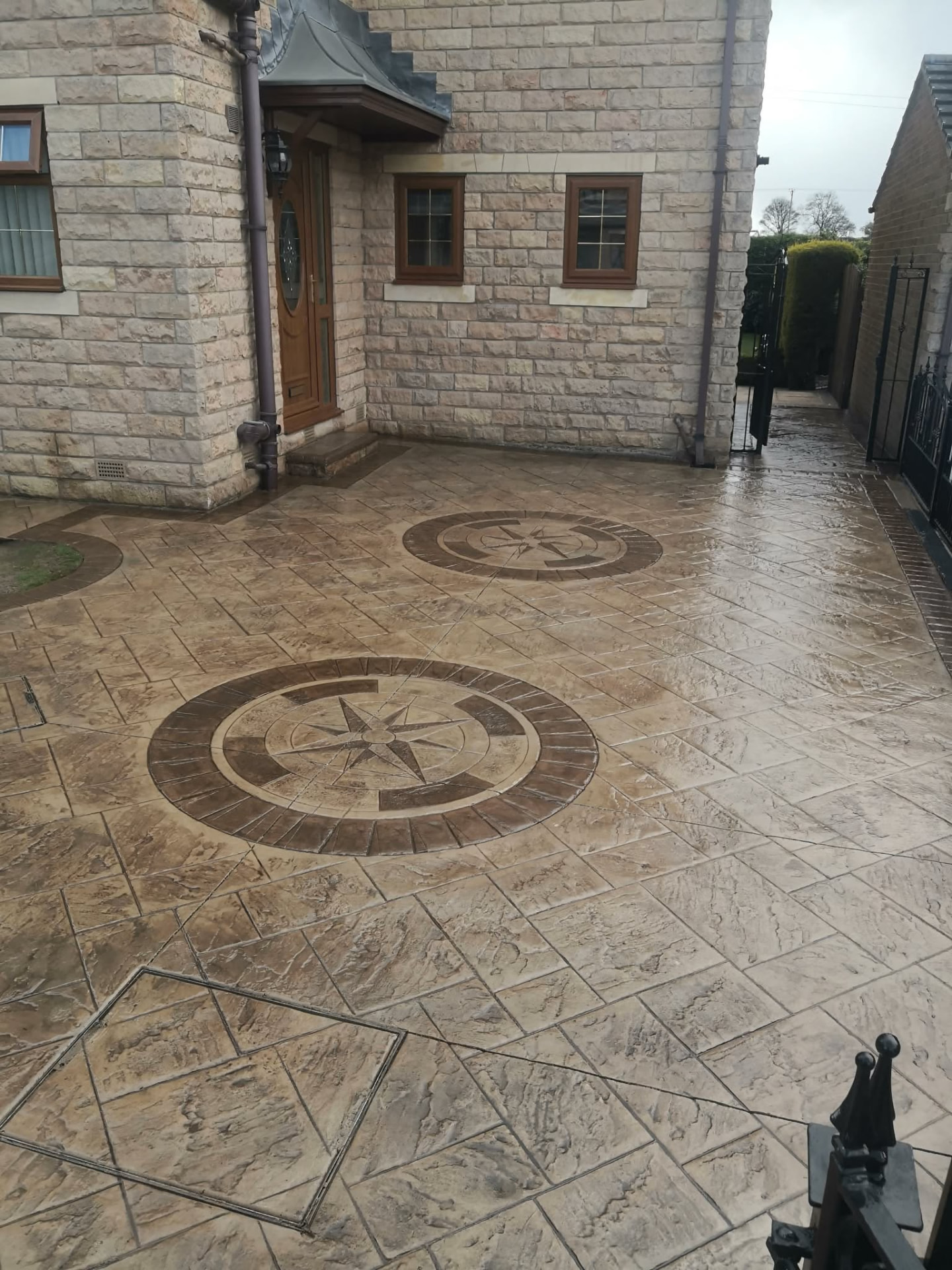 Buff pattern imprinted concrete patio with two compass rose features outside a stone house